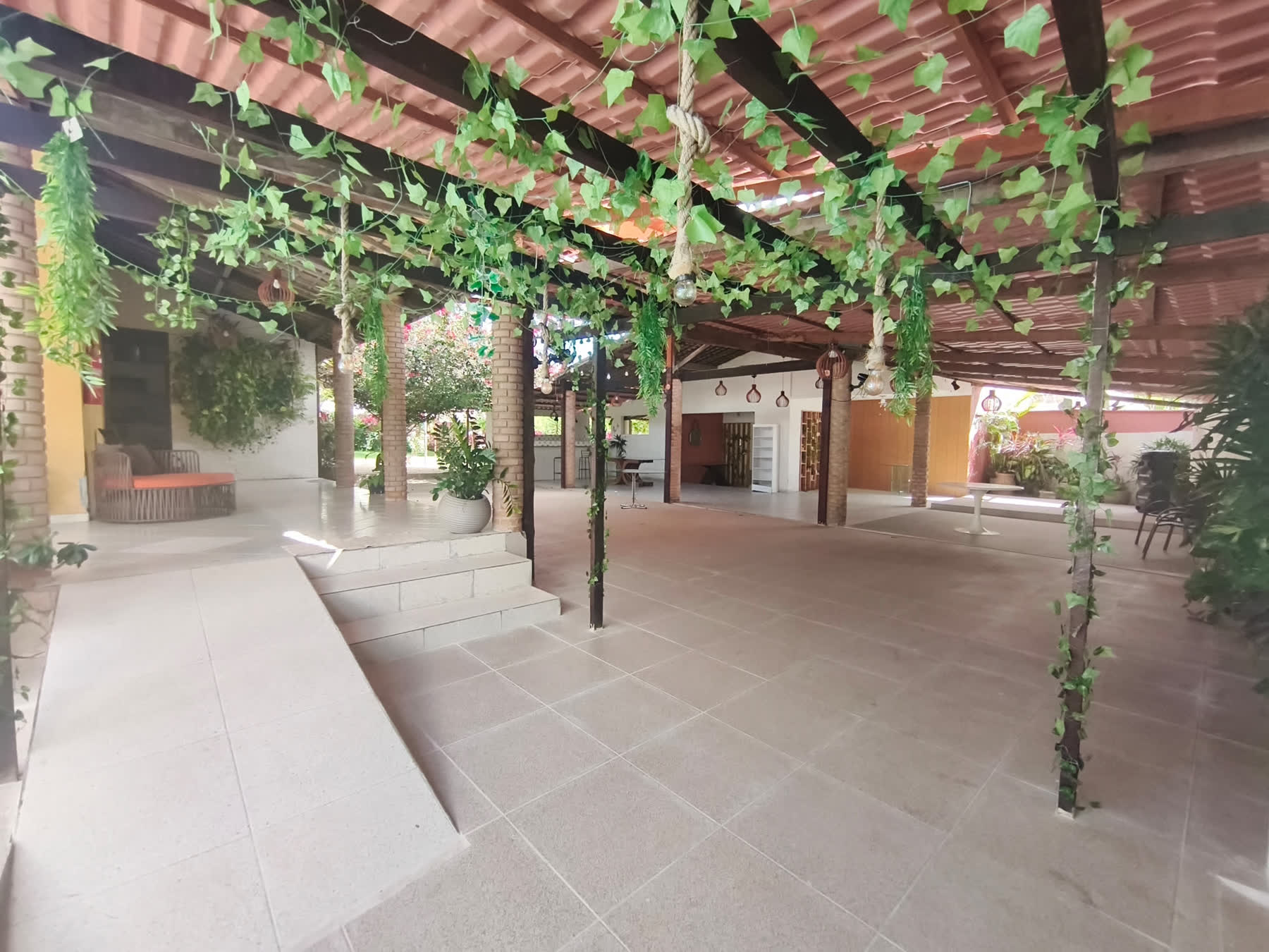 Área coberta integrada do Studio29 com colunas de tijolo e muito verde