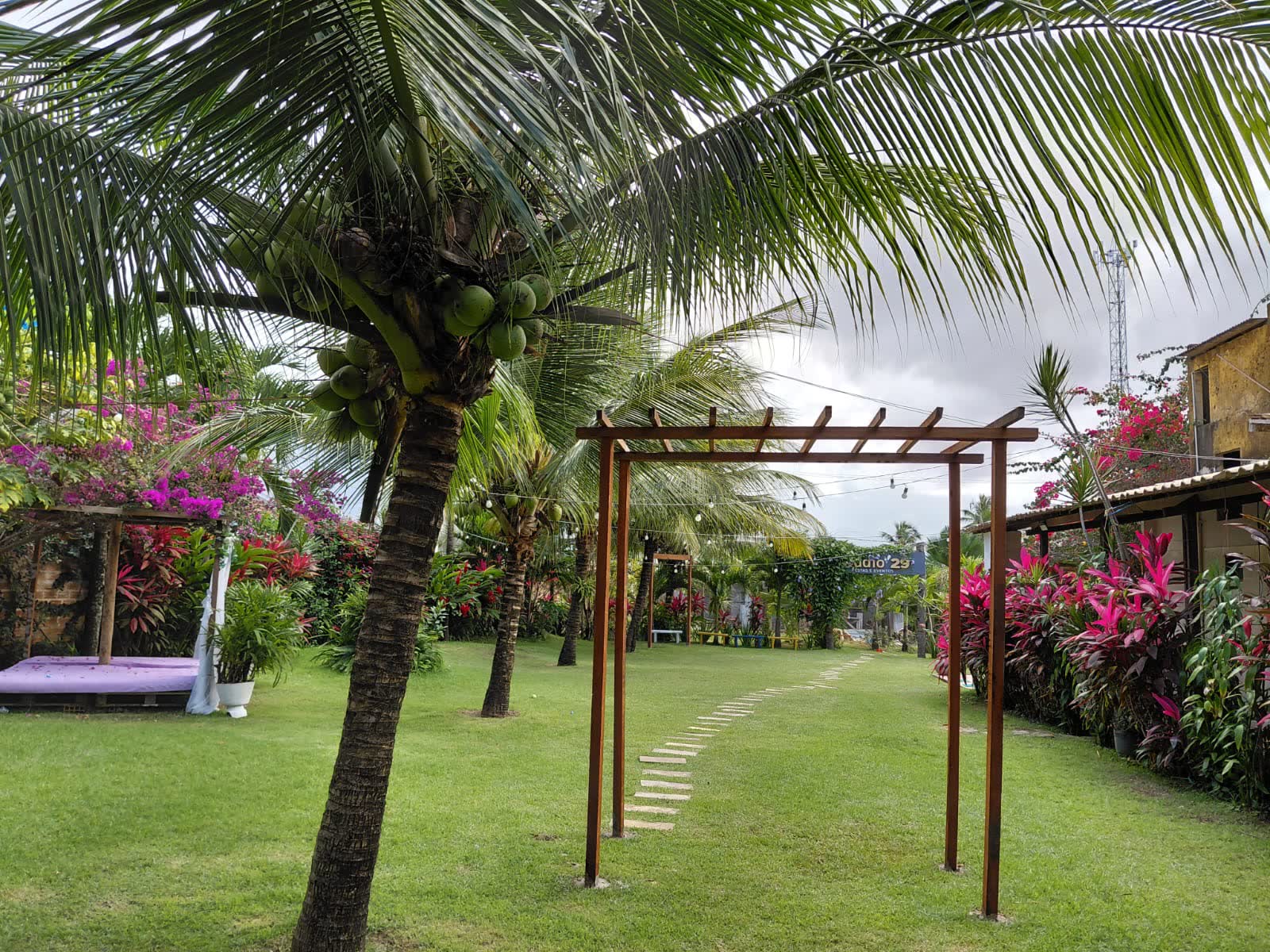 Pergolado de madeira no jardim do Studio29 entre coqueiros e folhagens coloridas