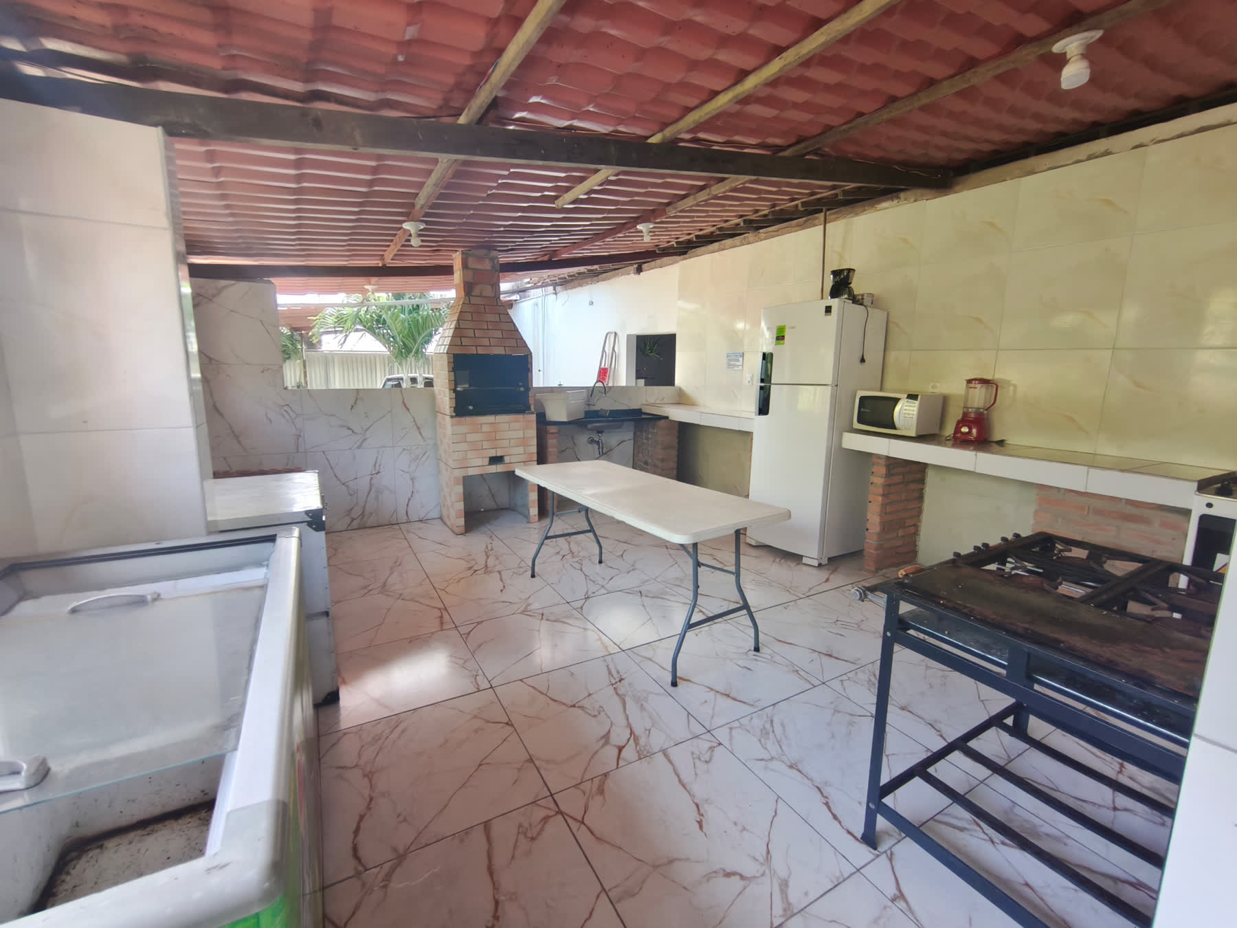 Cozinha do Studio29 com churrasqueira de tijolos, geladeira, fogão industrial e mesa de apoio