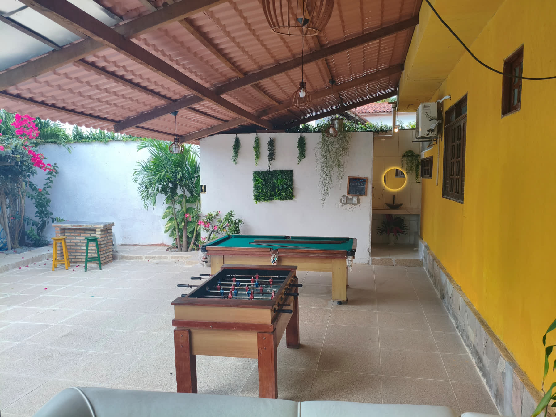 Área de lazer do Studio29 com mesa de sinuca, totó e parede de plantas
