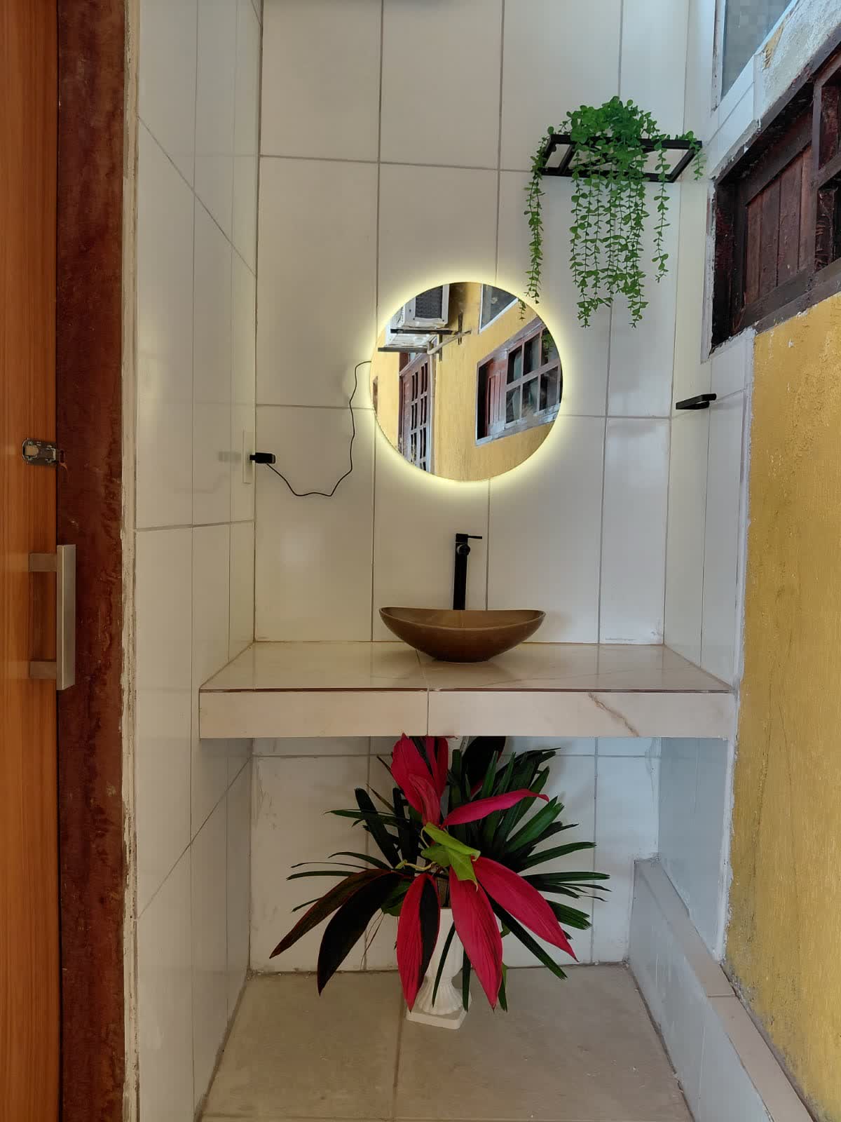 Lavabo do Studio29 com cuba de apoio, espelho redondo iluminado e planta