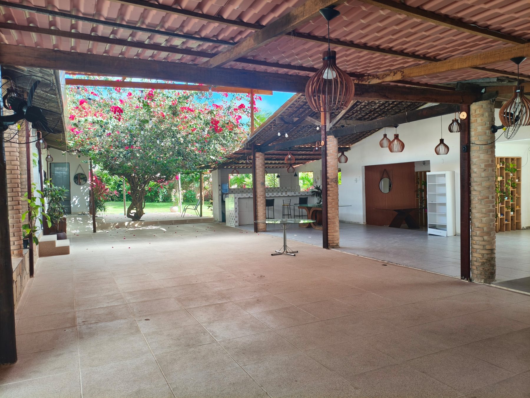 Pátio coberto do Studio29 com telhado de madeira, luminárias de fibra e árvore florida ao fundo